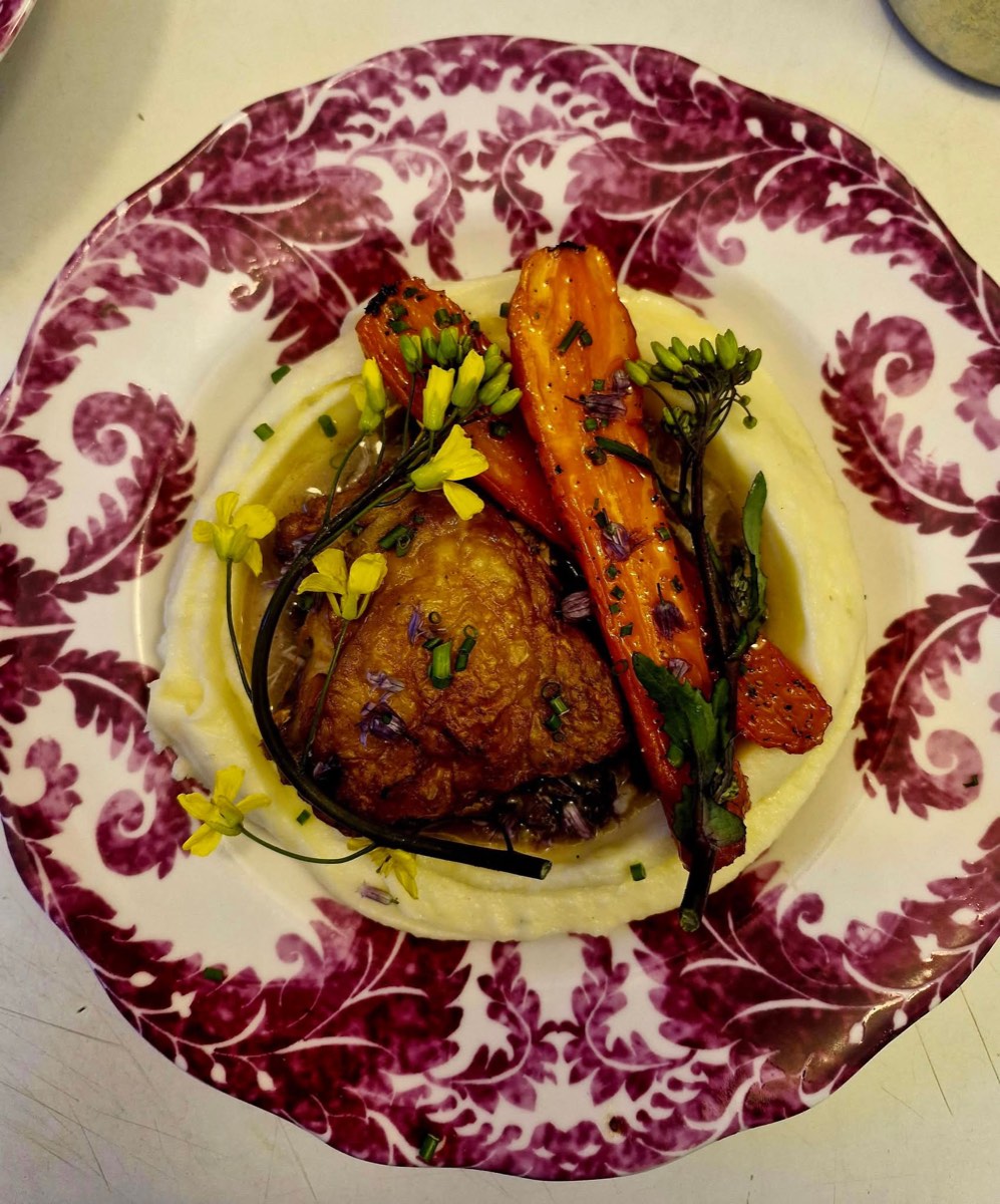 Crisp chicken thigh on buttery mash with roasted carrots and edible flowers