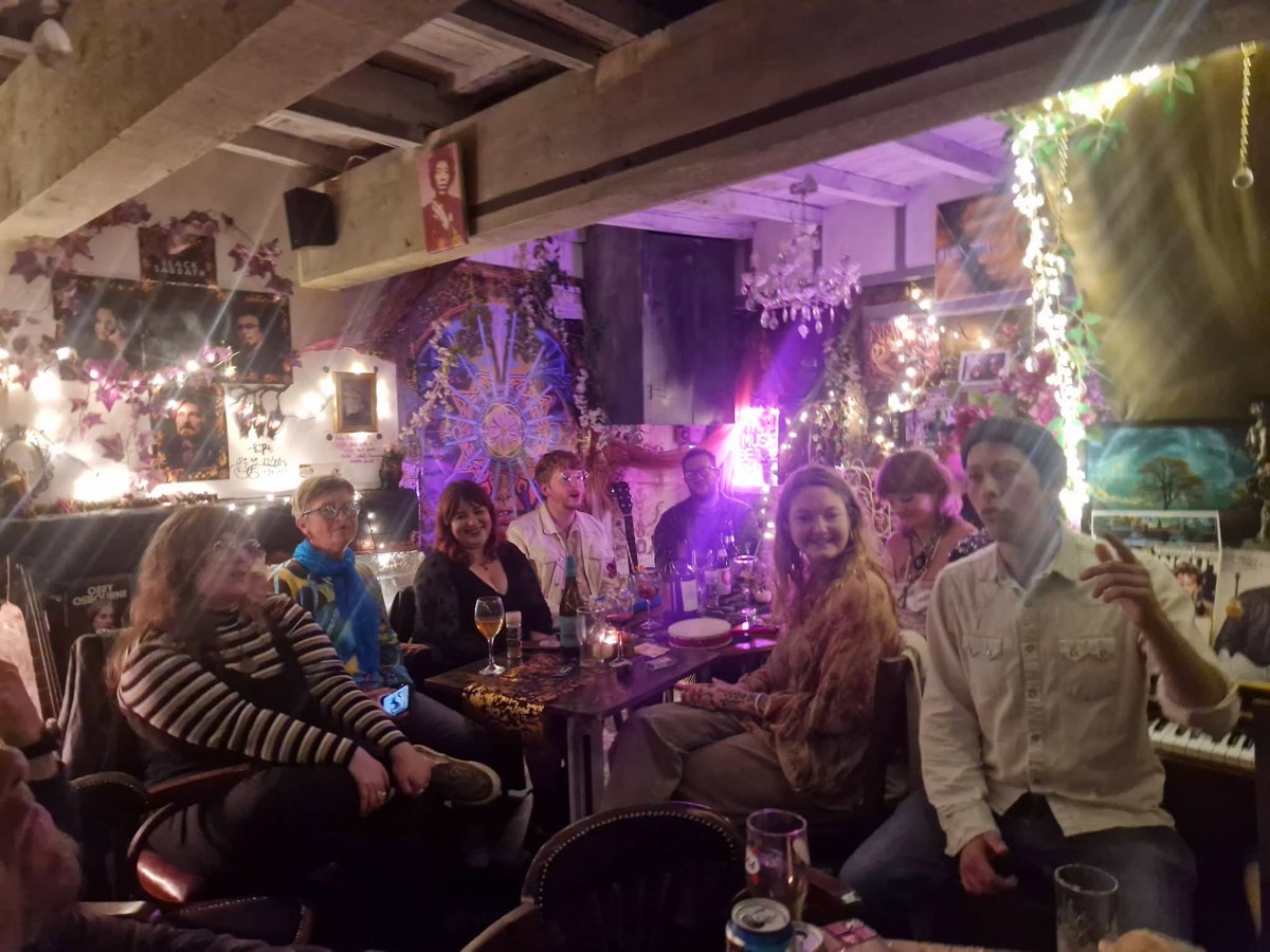 A full table on a music night under purple light and fairy lights