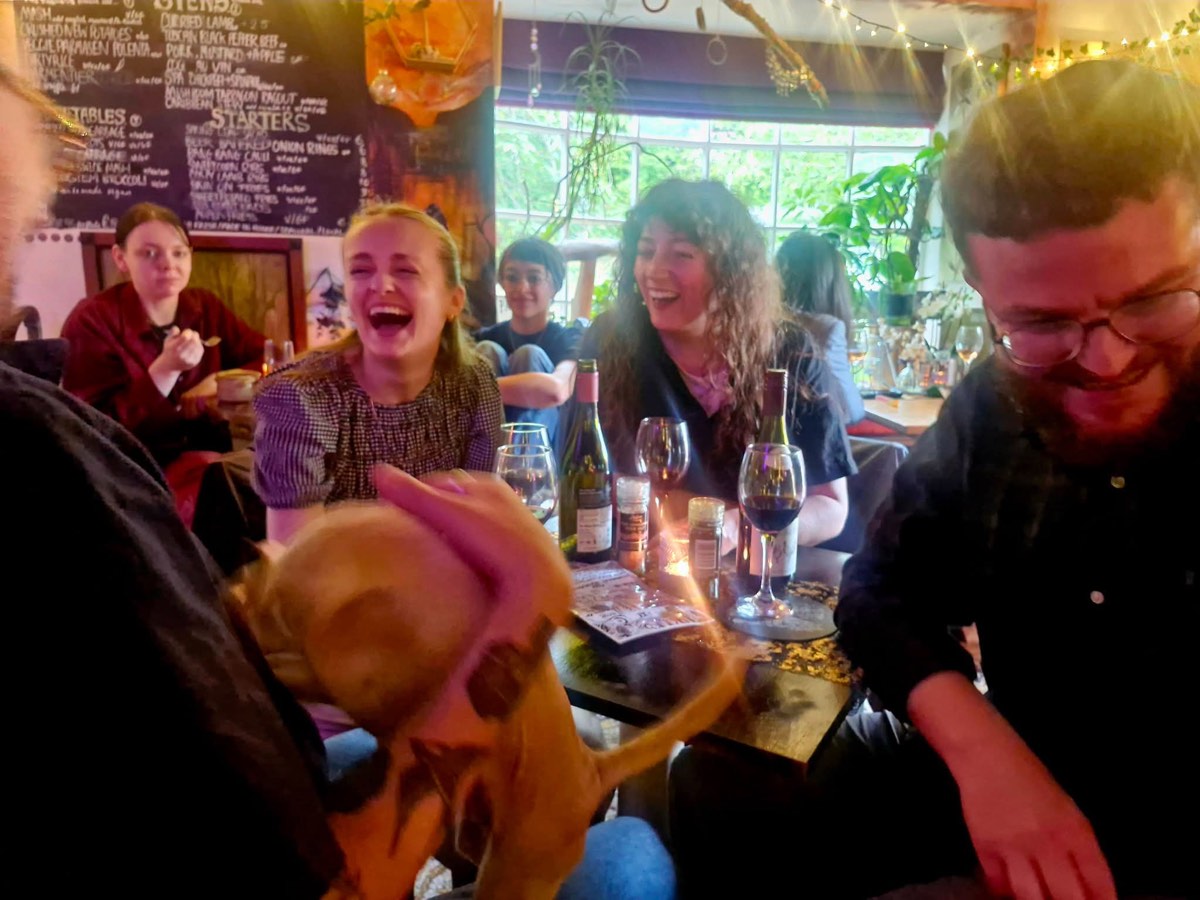 Friends laughing over wine with a dog joining in