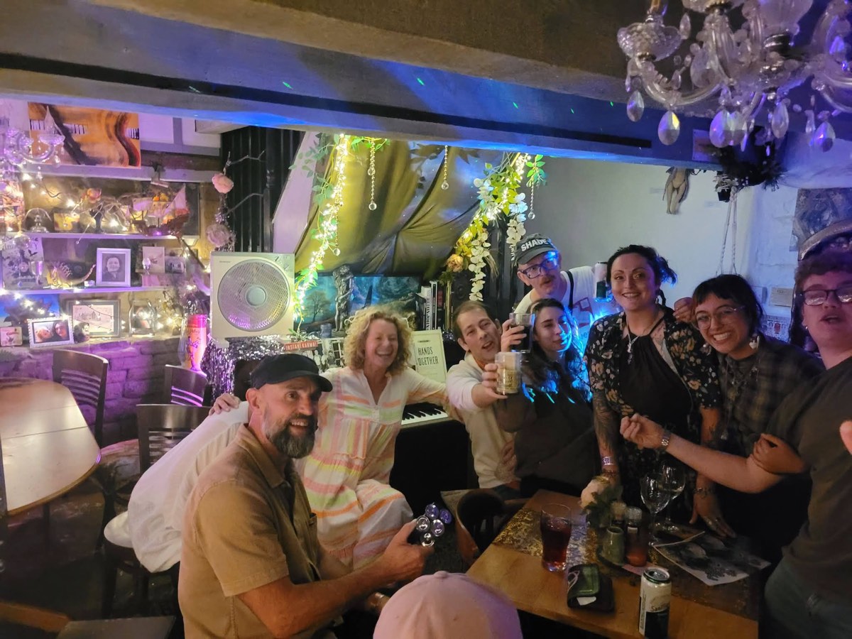 A birthday crowd gathered round the piano, drinks raised