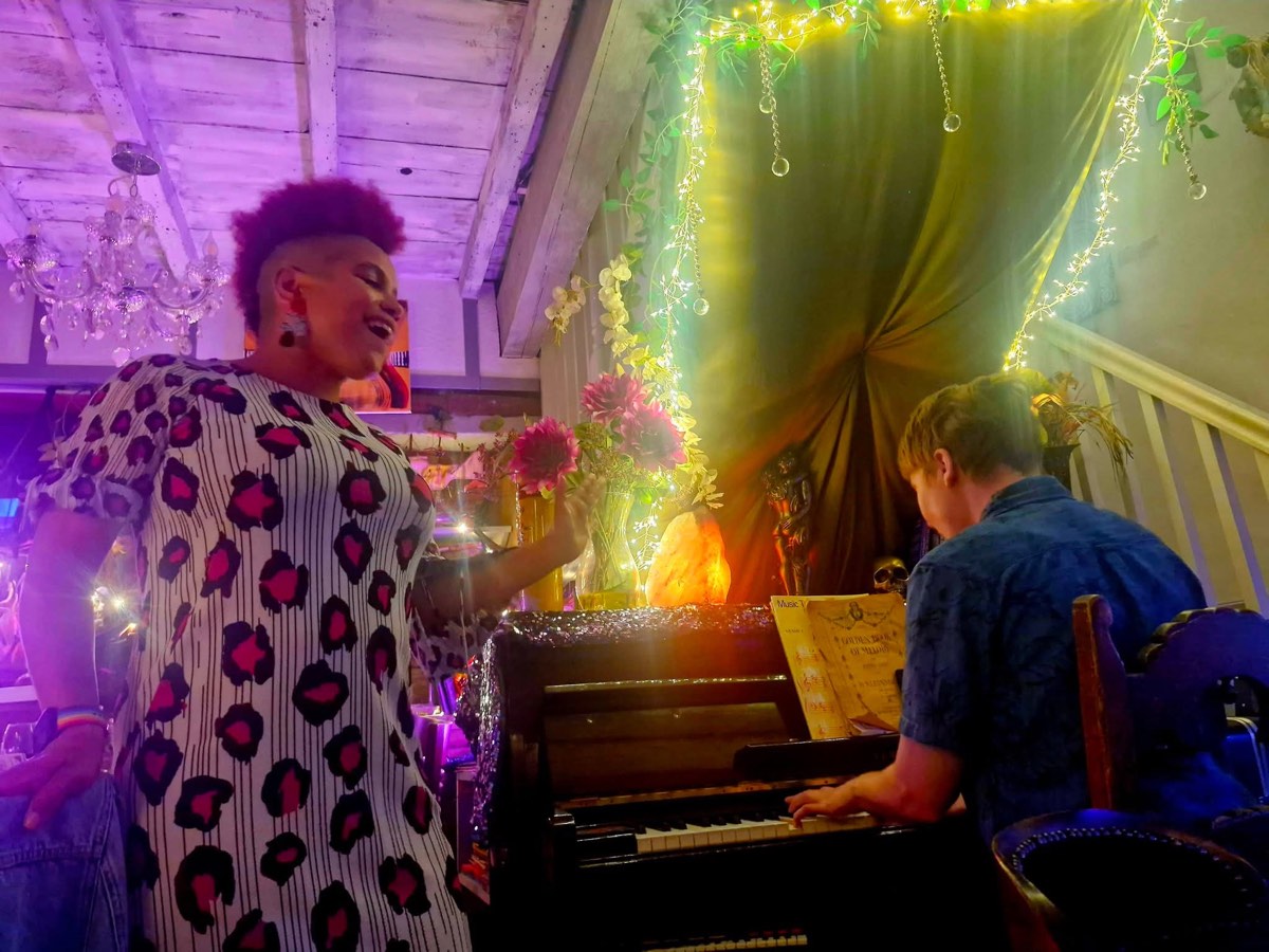 A singer performing beside the house piano, lit in purple and green